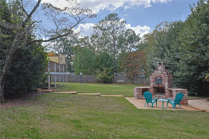Mature trees frame a sprawling grassy yard complete with a custom brick fireplace with pizza oven.