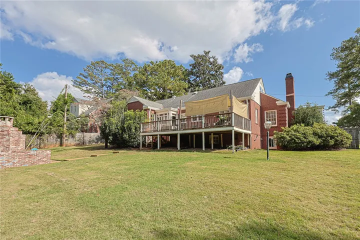 An expansive green lawn stretches toward the rear elevation featuring a prominent elevated wooden deck.