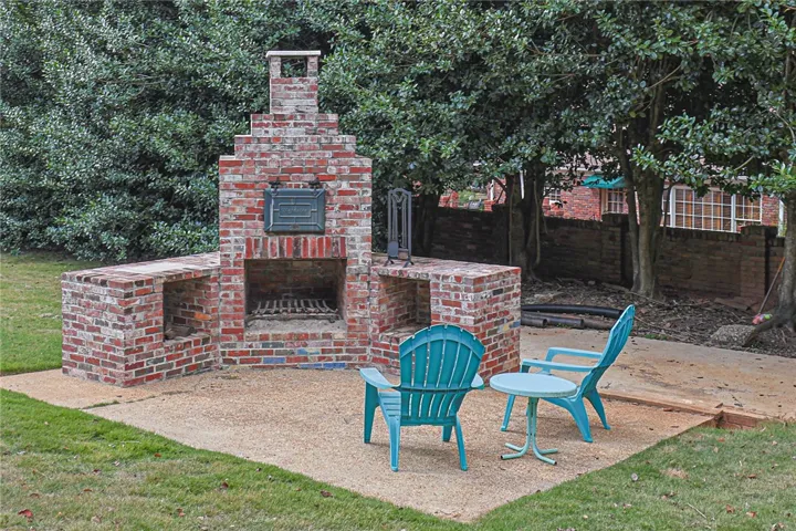 An impressive brick fireplace anchors the paved patio, nestled among mature trees.