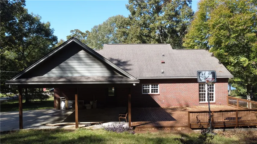 A spacious wooden deck extends from the brick exterior beneath mature shade trees.