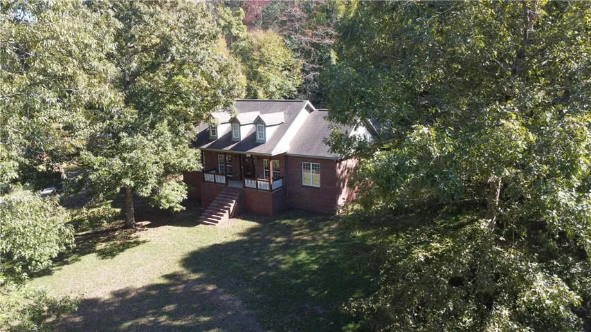 Thick mature trees frame this classic brick home nestled on a grassy lawn.