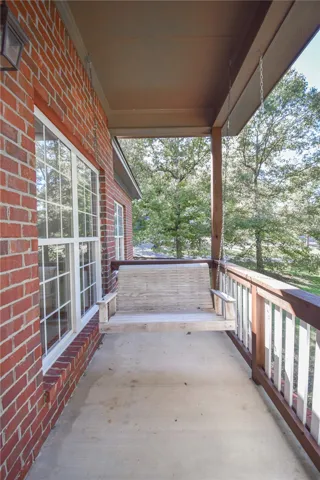 An inviting covered porch features solid concrete flooring, brick walls, and wooded neighborhood views.
