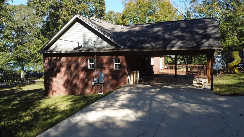 An attached brick carport opens to a concrete driveway framed by mature trees.