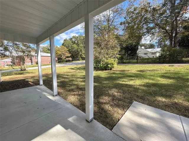 An inviting covered concrete patio looks out across a grassy, tree-lined yard.