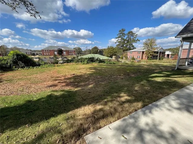 A spacious grassy lawn slopes gently away from the concrete patio under a blue sky.