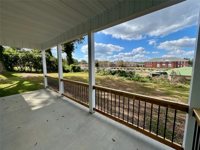 An elevated, covered porch with concrete flooring overlooks a grassy hillside and neighborhood views.
