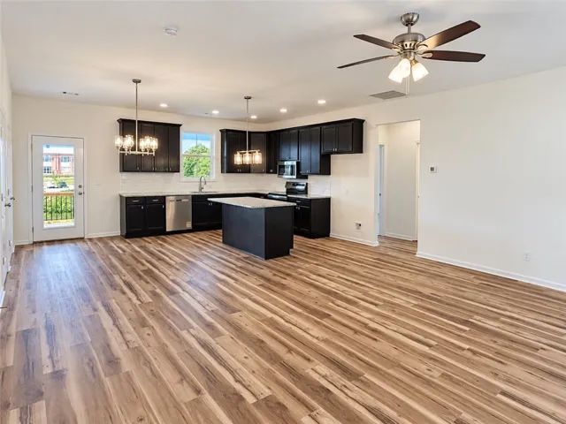 Rich wood-textured flooring flows seamlessly into an open kitchen with dark cabinetry and stone countertops.