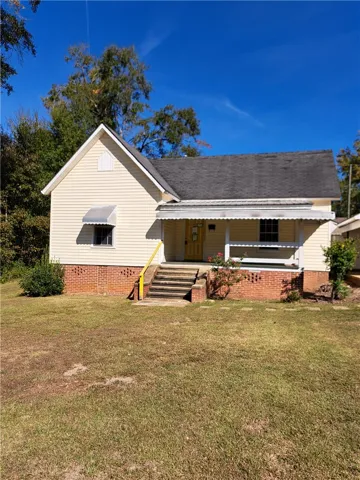 Classic vinyl and brick exterior features a covered front porch and mature surrounding trees.