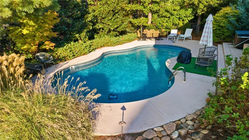 Lush mature trees surround a sparkling in-ground pool with ample concrete decking.