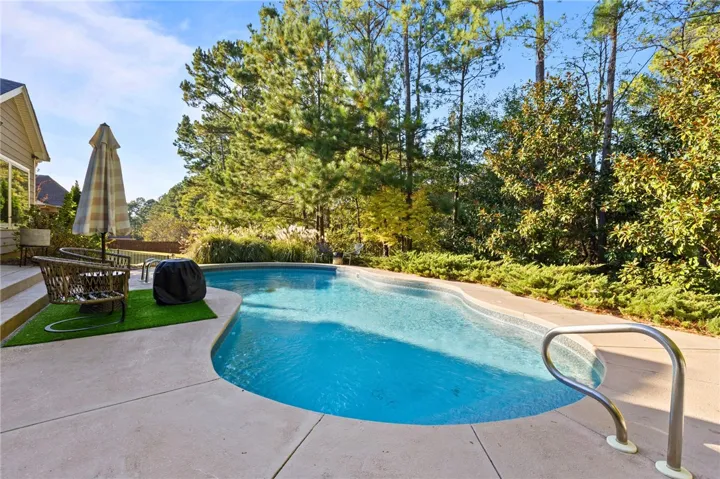 Mature trees frame a private in-ground pool and concrete patio in the backyard.