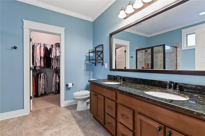Double vanities with stone countertops stand adjacent to a walk-in closet in this spacious bathroom.