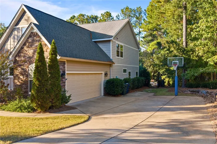 An inviting side view of the home features a stone facade, paved driveway, and basketball hoop.