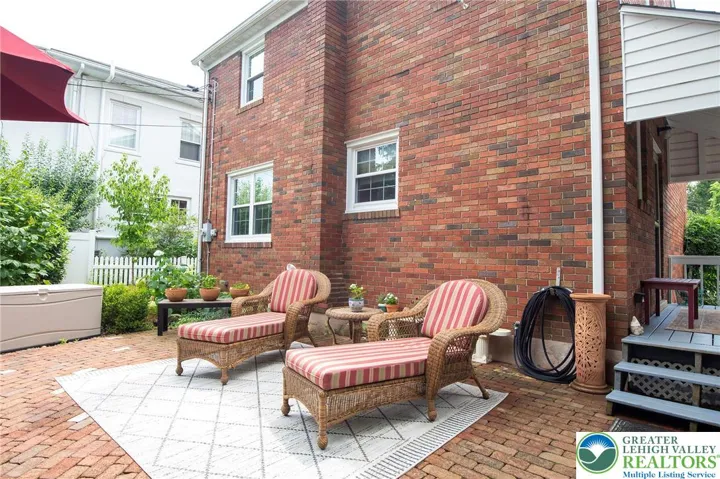 Spacious patio is surrounded by plantings, a veggie area, and shade trees.