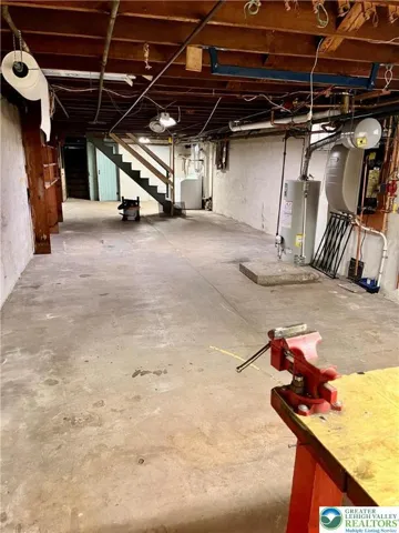 Spacious basement, heating system on wall beside water heater.