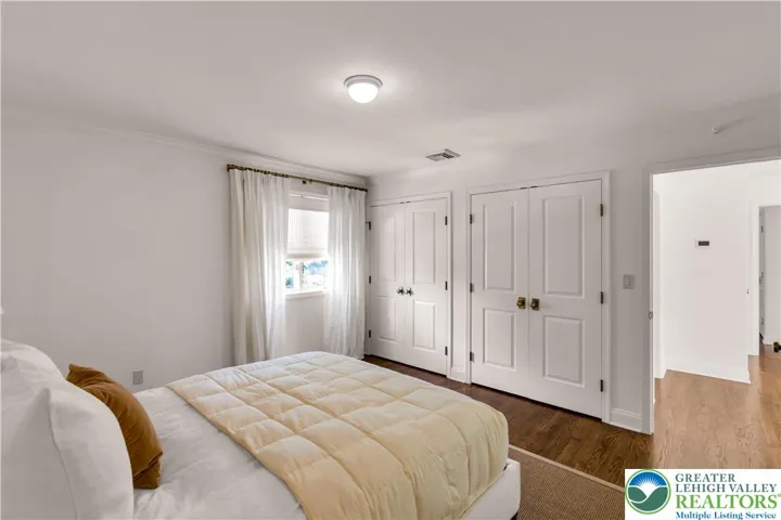 arge bedroom with hardwood flooring and closets featuring built-in storage—spacious, organized, and bright.