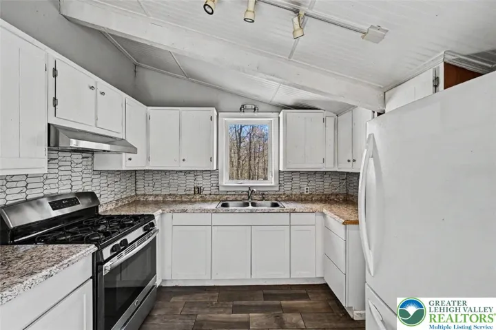The Kitchen features a vaulted ceiling with track lights and a window overlooking the back yard.
