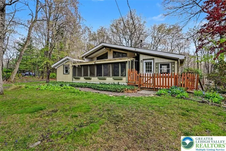 The home features mature flowering trees/plants and an inviting stone walkway to the deck and porch.
