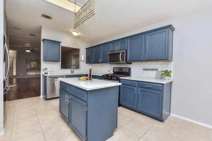 Kitchen with appliances with stainless steel finishes, light countertops, a kitchen island, and blue cabinetry