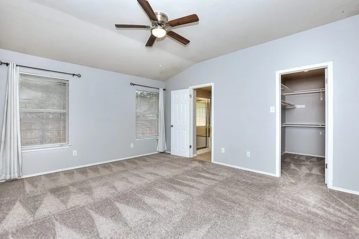 Unfurnished bedroom featuring connected bathroom, baseboards, vaulted ceiling, a spacious closet, and carpet