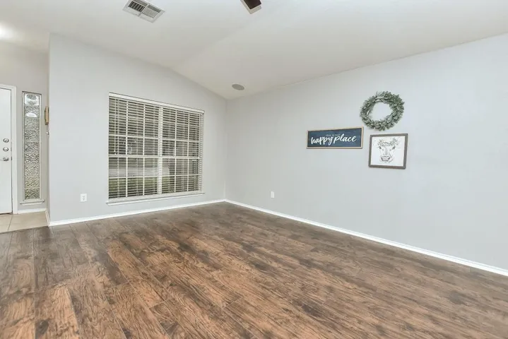 Empty room with dark wood-type flooring, lofted ceiling, visible vents, and baseboards