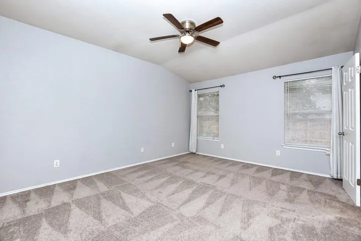 Spare room with lofted ceiling, ceiling fan, light carpet, and baseboards
