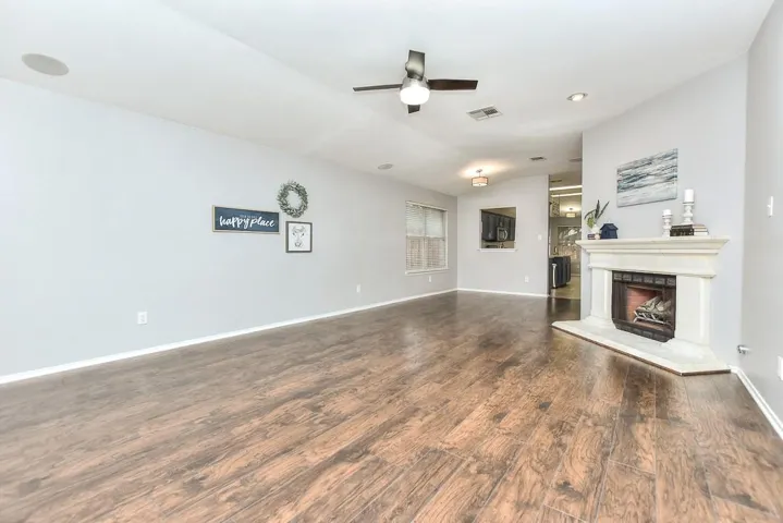 Unfurnished living room with a fireplace with raised hearth, ceiling fan, lofted ceiling, visible vents, and dark wood finished floors