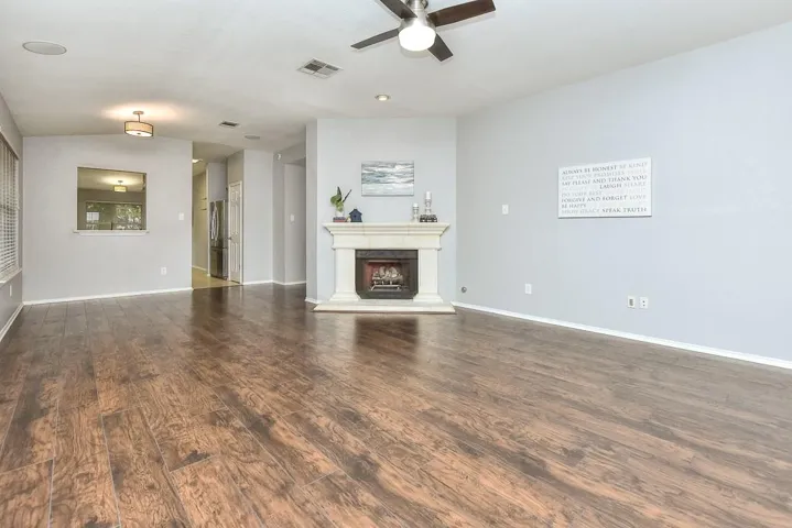 Unfurnished living room with dark wood-style flooring, a fireplace with raised hearth, visible vents, and baseboards