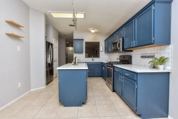 Kitchen featuring light tile patterned floors, a center island with sink, appliances with stainless steel finishes, light countertops, and blue cabinetry