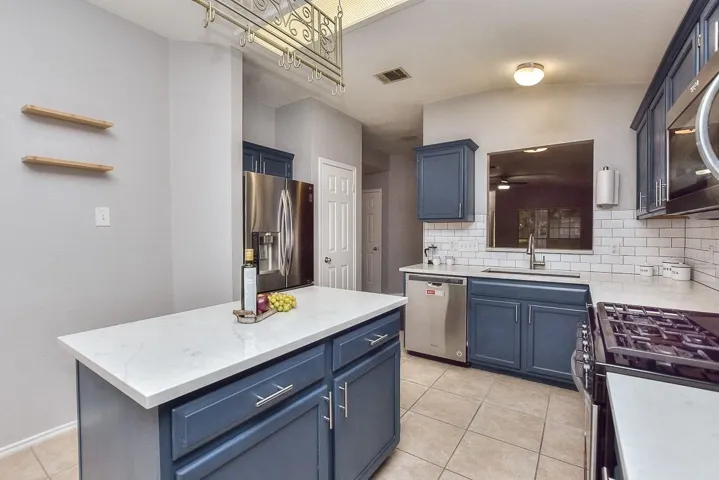 Kitchen with blue cabinets, stainless steel appliances, a kitchen island, a sink, and visible vents