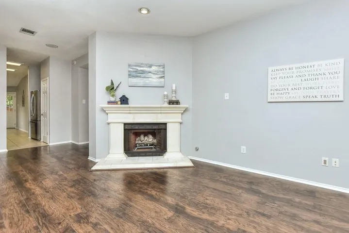 Unfurnished living room with a fireplace with raised hearth, visible vents, baseboards, and wood finished floors