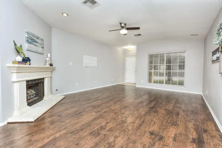 Unfurnished living room with a fireplace with raised hearth, ceiling fan, wood finished floors, visible vents, and vaulted ceiling