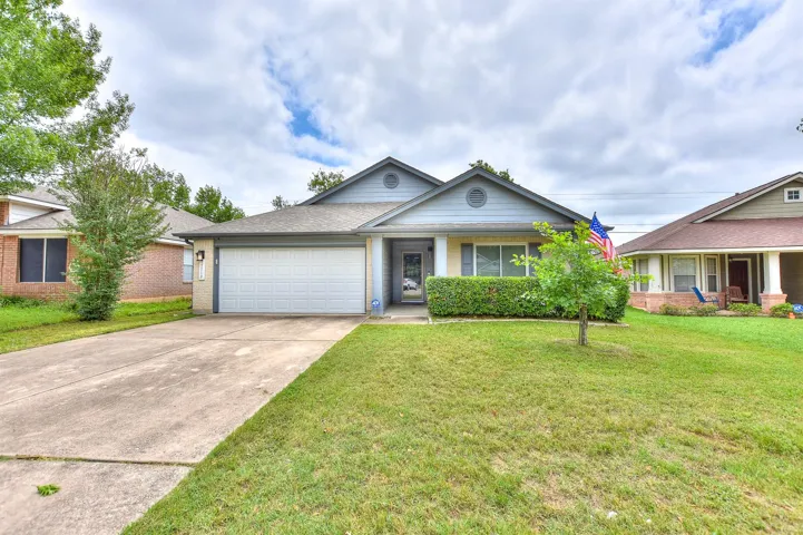 Ranch-style home featuring a garage, concrete driveway, a front lawn, brick siding, and roof with shingles
