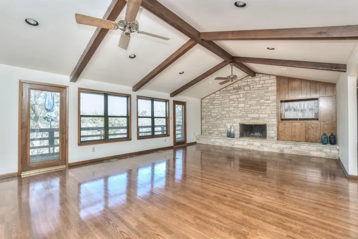 Unfurnished living room featuring a fireplace, vaulted ceiling with beams, a ceiling fan, and a wealth of natural light