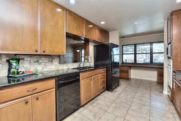 Kitchen featuring baseboards, decorative backsplash, brown cabinets, black appliances, and a sink