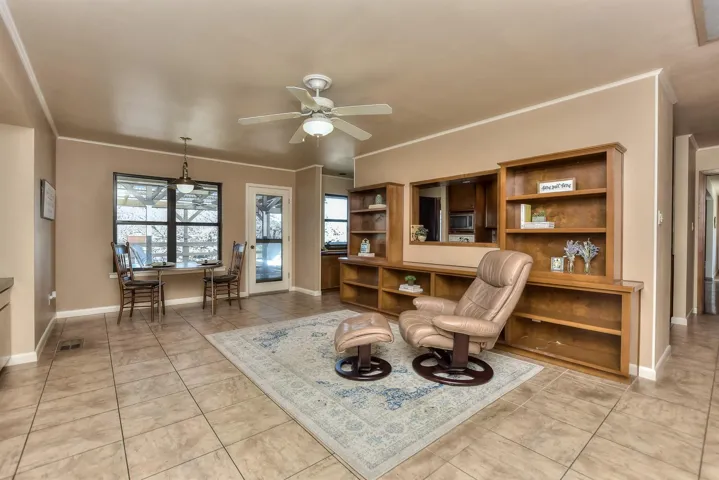 Living area with light tile patterned floors, visible vents, ceiling fan, and ornamental molding