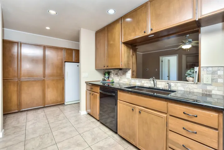 Kitchen featuring a ceiling fan, a sink, black dishwasher, freestanding refrigerator, and brown cabinetry