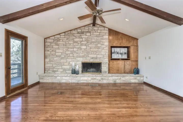 Unfurnished living room featuring a large fireplace, lofted ceiling with beams, a ceiling fan, and wood finished floors