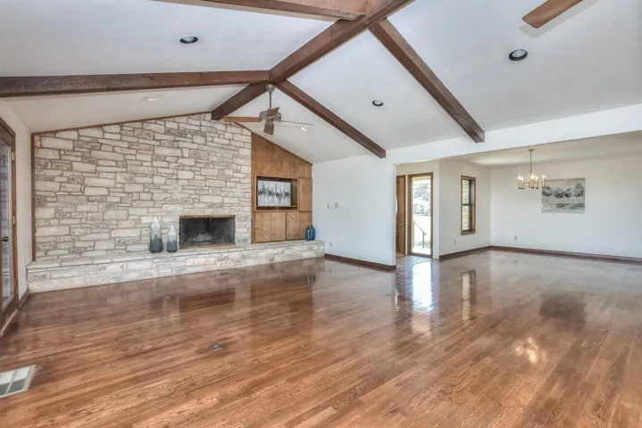 Unfurnished living room with visible vents, ceiling fan with notable chandelier, lofted ceiling with beams, wood finished floors, and a fireplace