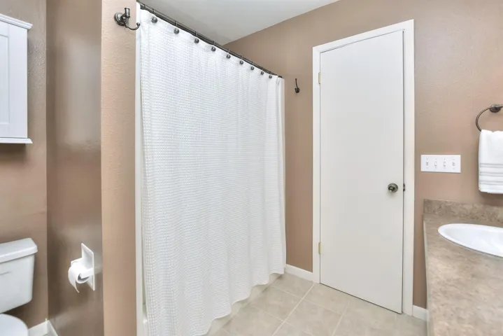 Full bathroom featuring tile patterned flooring, toilet, a shower with shower curtain, and a sink