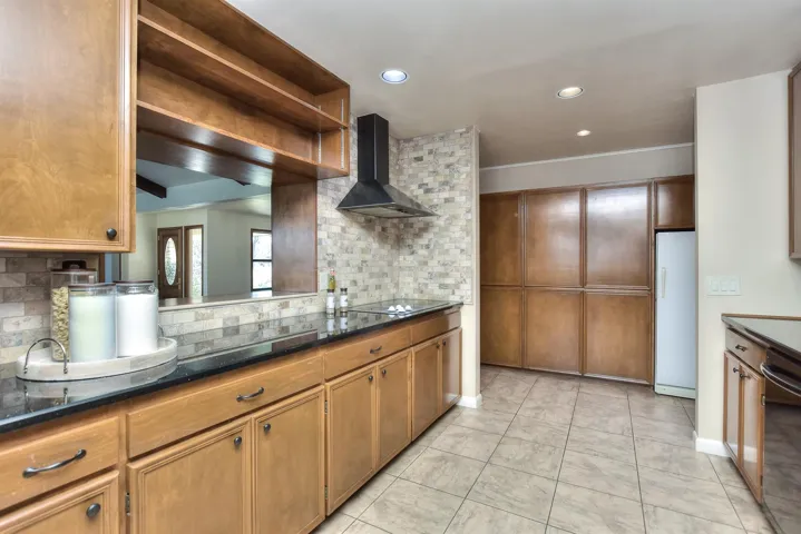 Kitchen featuring backsplash, wall chimney range hood, light tile patterned floors, black appliances, and open shelves