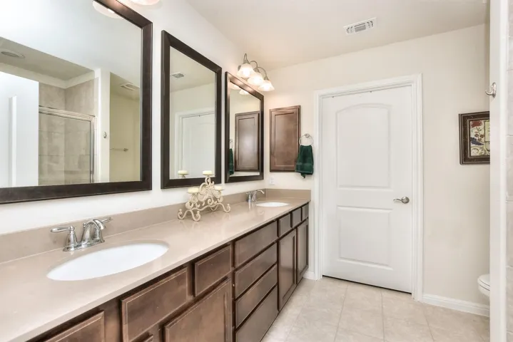Bathroom with tile patterned flooring, tiled shower, visible vents, and a sink