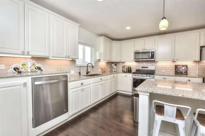Kitchen featuring dark wood finished floors, a sink, white cabinets, appliances with stainless steel finishes, and backsplash