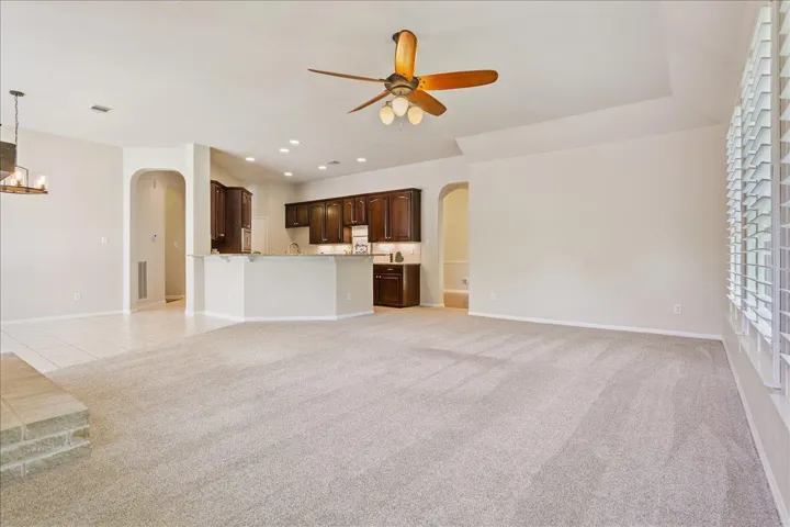 Unfurnished living room featuring arched walkways, ceiling fan, light colored carpet, a chandelier, and recessed lighting