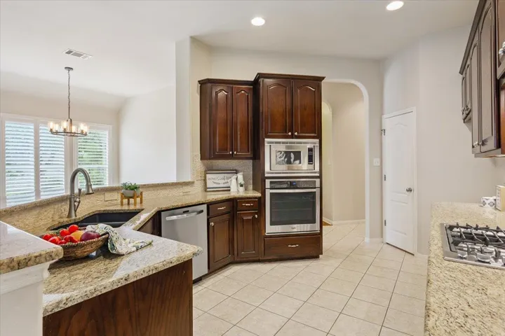 Kitchen with stainless steel appliances, backsplash, a chandelier, light stone countertops, and light tile patterned floors