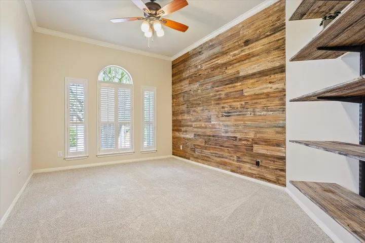 Spare room with wood walls, crown molding, carpet flooring, a ceiling fan, and an accent wall