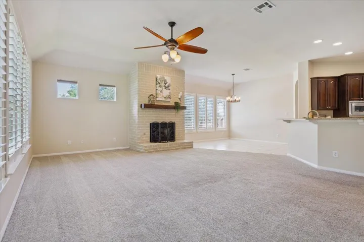 Unfurnished living room with ceiling fan, a brick fireplace, recessed lighting, light carpet, and a chandelier