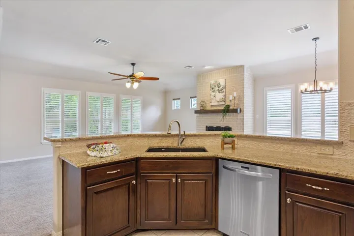 Kitchen with dishwasher, ceiling fan, light stone counters, a chandelier, and light colored carpet