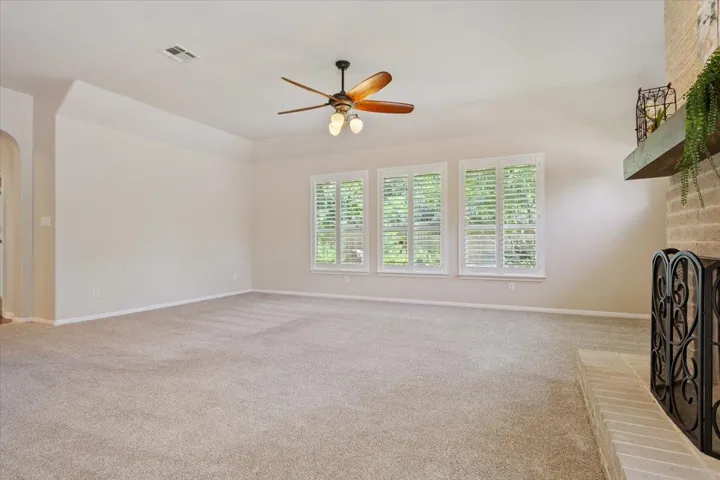 Unfurnished living room featuring a brick fireplace, arched walkways, ceiling fan, and carpet floors