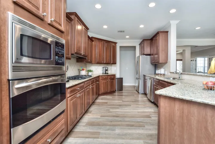 Kitchen featuring stainless steel appliances, decorative backsplash, a sink, light stone counters, and visible vents