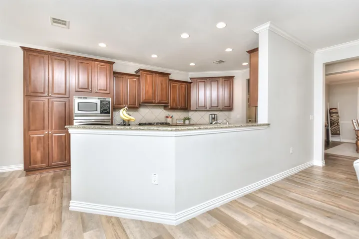 Kitchen with backsplash, light wood finished floors, brown cabinetry, stainless steel microwave, and visible vents